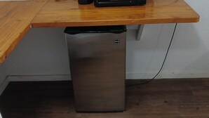 Un refrigerador compacto con pantalla digital, ubicado debajo de una mesa de madera en una habitación con piso de madera oscura.