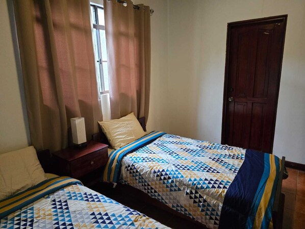 A bedroom with two beds, a wooden door, and a window with curtains. - Hostal Casa San Mateo (León)