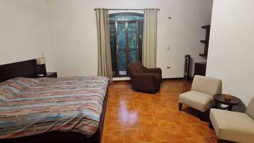 Habitación de hotel con cama, una silla, una mesita y ventana con cortinas.