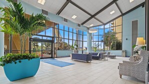 Een ruime lobby met een grote blauwe plantenbak, comfortabele zithoeken en grote ramen met uitzicht op buiten.