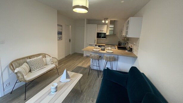 A modern living room with a sofa, a coffee table, and a dining area with chairs and a kitchen in the background. - Charming, quiet flat in Arcachon (Arcachon)