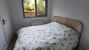 A small bedroom with a single bed, a window with a view of a wooden deck, and a white radiator below the window. - Charming, quiet flat in Arcachon (Arcachon)