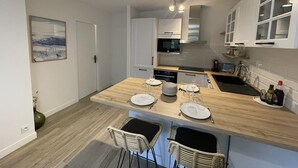 A modern kitchen with a wooden island, white cabinetry, and a dining area with two wicker chairs. - Charming, quiet flat in Arcachon (Arcachon)
