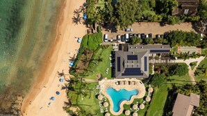 Una vista aerea di un resort con piscina, spiaggia e vegetazione lussureggiante.