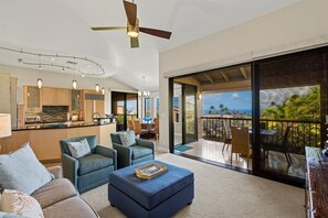 A modern living room with a sofa, ottoman, and a dining area with chairs. A kitchen is visible in the background. - Modern Spacious Beachfront Luxury in Wailea. Family Friendly! (Kihei)
