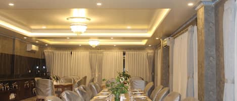 Una larga mesa de comedor dispuesta para una comida formal, con sillas a ambos lados, en una habitación bien iluminada con candelabro y cortinas.