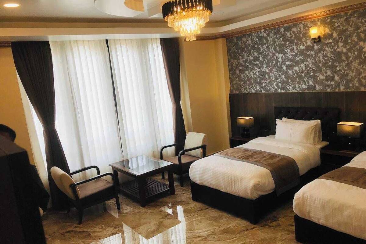 Une chambre d’hôtel avec deux lits, une petite table, des chaises, un lustre et un mur décoratif.