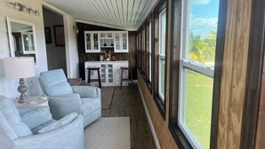 A modern living room with a grey sofa, a small table with a lamp, and a view of a kitchen with white cabinets and a wooden wall. - Spacious 5-bedroom ocean view house in marvelous Green Turtle Cay with WiFi, AC (Green Turtle Cay)