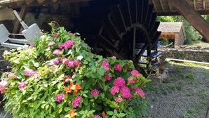 A rustic stone structure with a water wheel, surrounded by lush greenery and pink flowers. - Charming gîte in the heart of a water mill. 40 minutes from Le Mans and 15 minutes from Le Perche (Moncé-en-Saosnois)