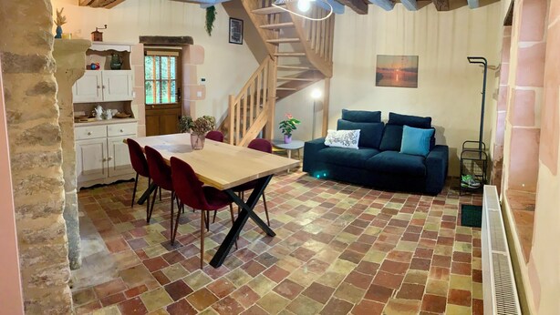 A cozy living room with a wooden staircase, a dining area with a table and chairs, and a blue sofa. - Charming gîte in the heart of a water mill. 40 minutes from Le Mans and 15 minutes from Le Perche (Moncé-en-Saosnois)