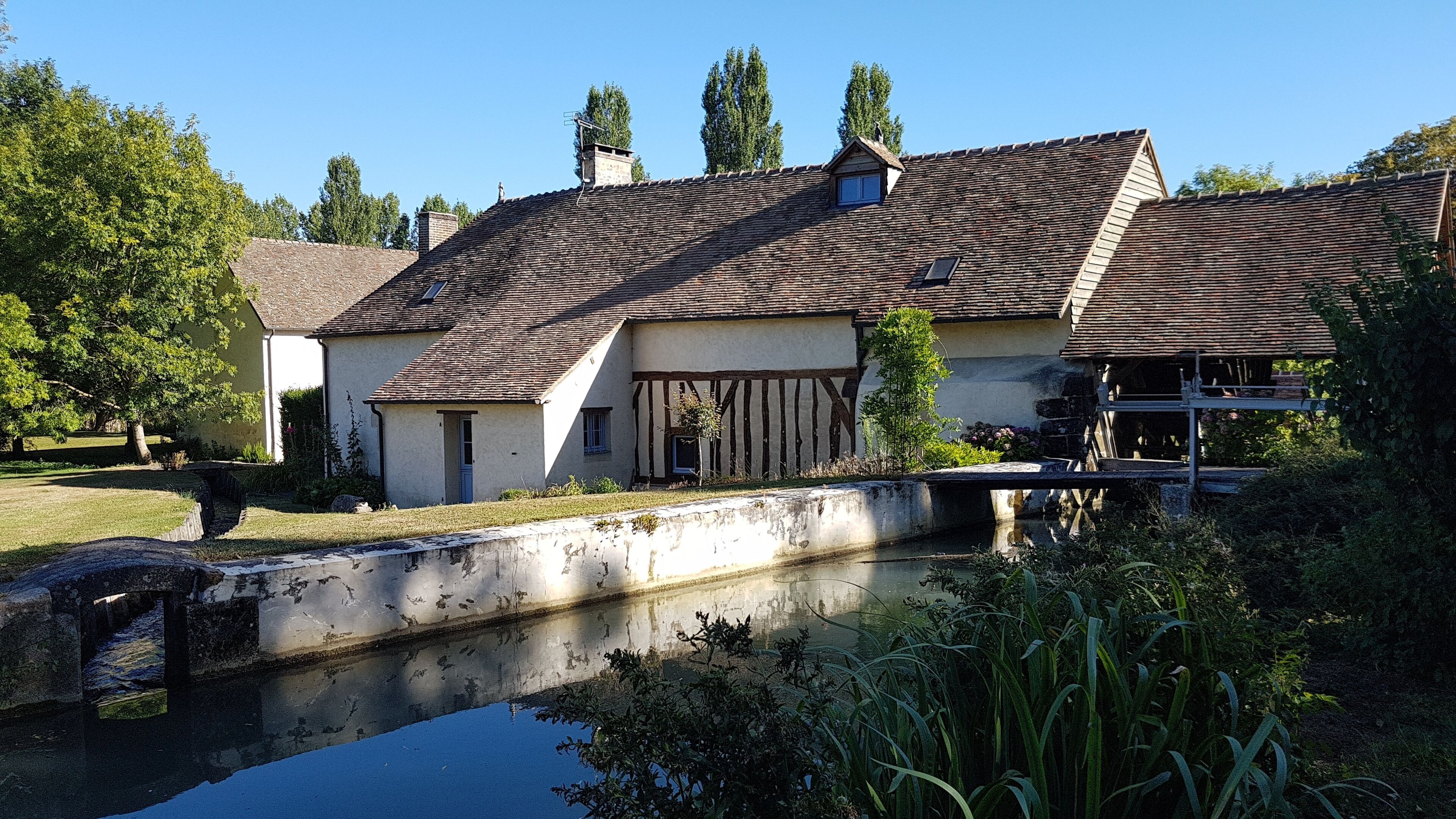 A traditional building with a tiled roof, a small pond in front, and a bridge over the water.