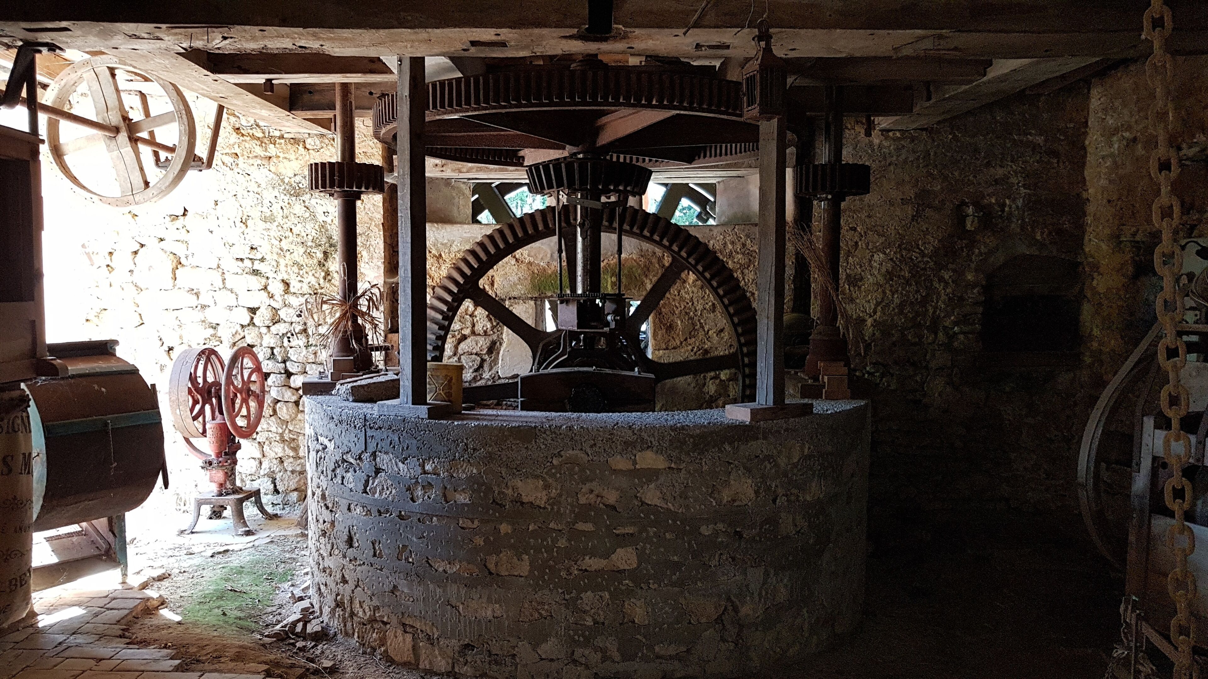 Une grande roue à eau mécanique, installée dans un bâtiment en pierre dont l’intérieur est de style rustique.