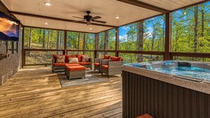 A covered outdoor area with a hot tub, wicker furniture, and a view of a forest. - Hidden Haven, Hot Tub, FREE Attraction tickets each paid day, Game Room, WIFI!!! (Sevierville)