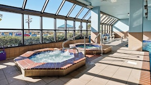 Ett poolområde på taket med två bubbelpooler, ett glastak och utsikt över en nöjespark.