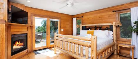 A wooden cabin bedroom with a fireplace, a bed, and a ceiling fan.