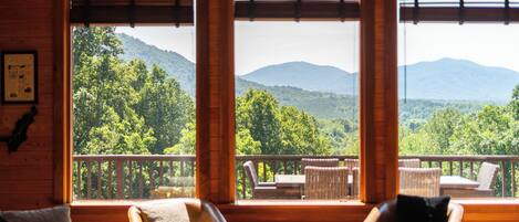A cozy living room with a large window, a ceiling fan, and a view of a forested mountain range.