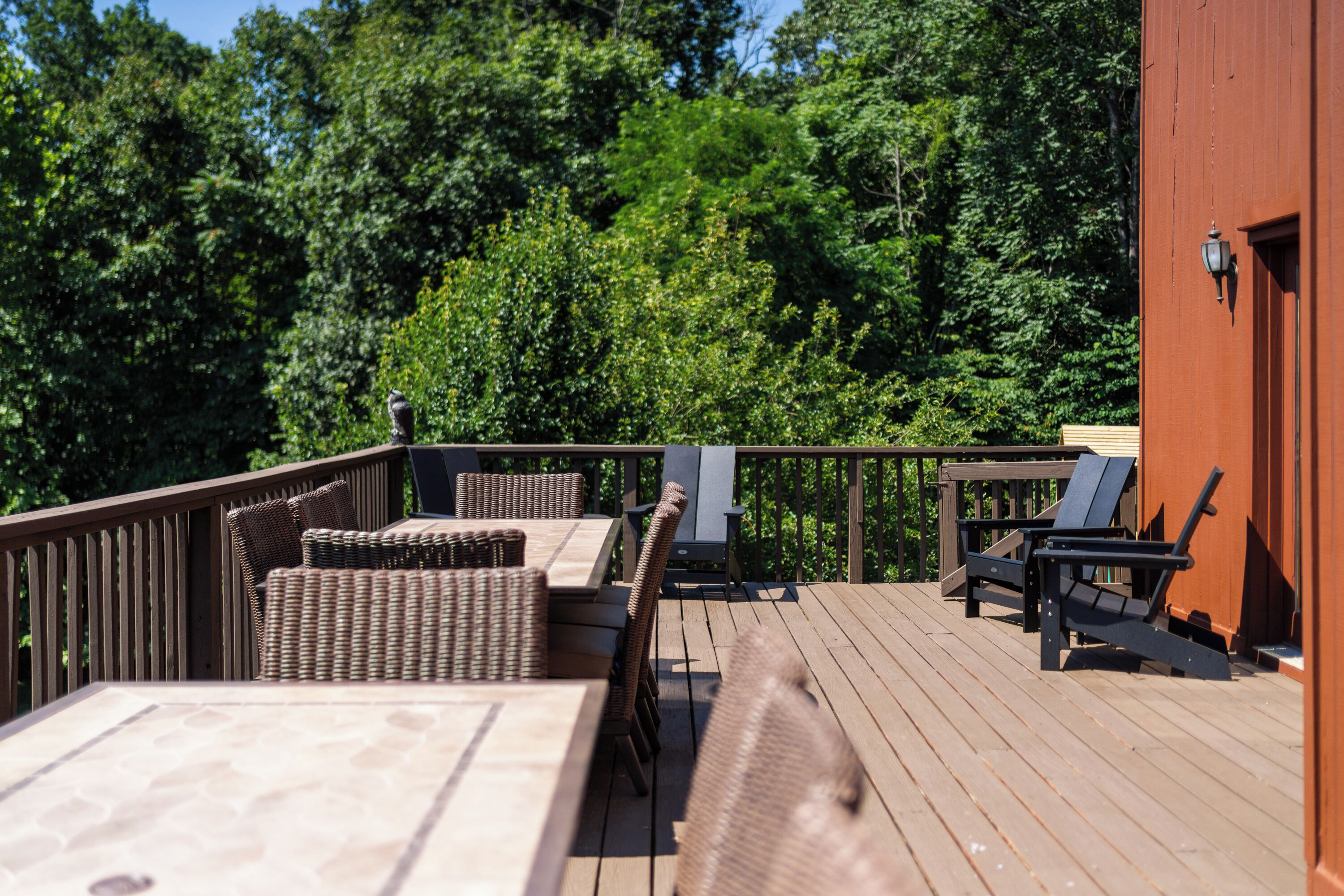 A wooden deck with wicker furniture and a red building in the background.