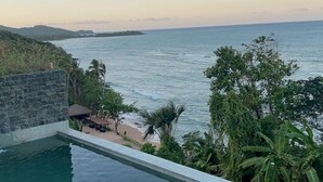 Una piscina con vistas al océano y una zona de playa con sombrillas.