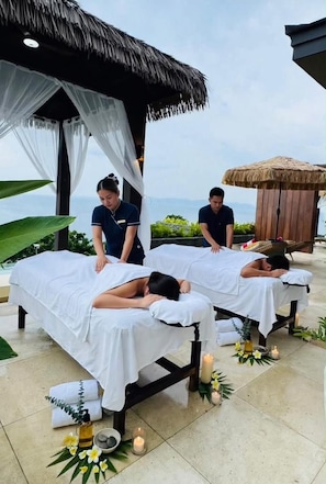 Een massagesalon met twee massagetafels, een rieten dak en uitzicht op de oceaan.