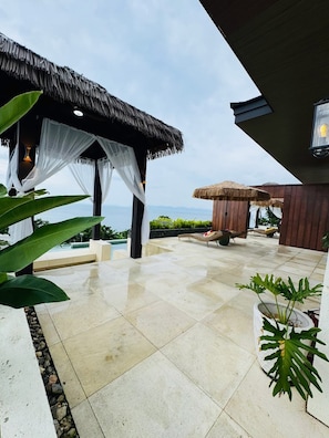 A covered outdoor area with a pool, lounge chairs, and a view of the ocean.