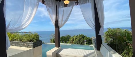 Un área de estar privada al aire libre con piscina, cortinas blancas y vistas al mar.