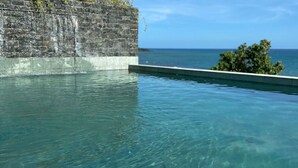 Piscina cristalina con pared de piedra y vista al océano.