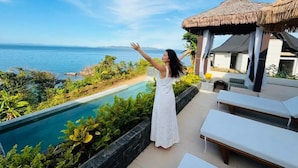 Una mujer con un vestido blanco parada junto a una piscina con vista al océano.