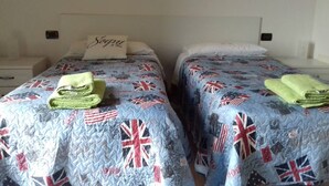 Due letti singoli con biancheria azzurra coordinata con motivi Union Jack, cuscini con il nome "Sophie" e asciugamani verdi ordinatamente piegati su ogni letto.