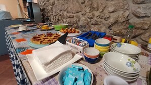 Un tavolo da buffet con diversi cibi e piatti, tra cui un piatto di lasagna, una ciotola di insalata e diverse pile di piatti bianchi con decorazioni floreali.