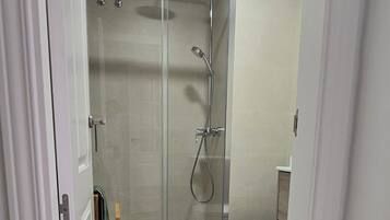 A modern bathroom with a glass shower enclosure, a toilet, and a wooden ladder.