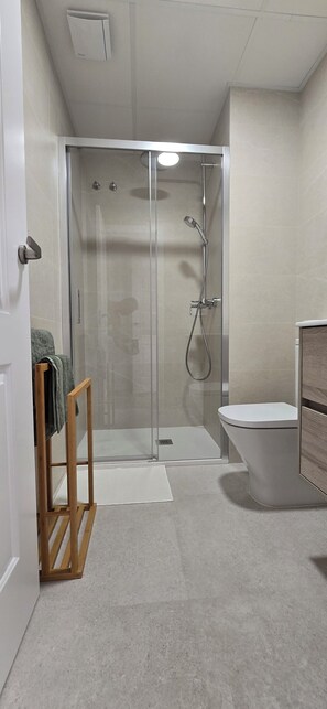 A modern bathroom with a glass-enclosed shower, a toilet, and a wooden towel rack.