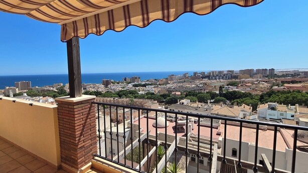 Un balcón con vista a un paisaje urbano costero, que incluye edificios y el mar.