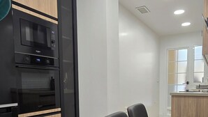 Una cocina moderna con armarios negros y de madera, un microondas integrado y una zona de comedor con mesa de madera y sillas negras.