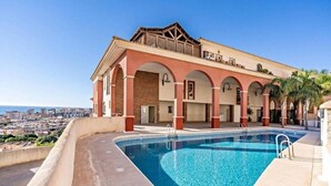 Un hotel con piscina, vistas a la ciudad y un balcón con palmeras.