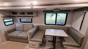A compact RV interior with a sofa, a table, and a window providing a view of greenery. - Cozy RV with terrific views, and peaceful surroundings. (Ukiah)