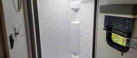 Un baño con ducha, inodoro y ventana con persianas.