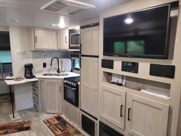 A compact kitchen with a stove, sink, and a large flat-screen TV mounted on the wall.