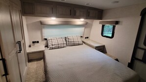 A compact RV bedroom with a bed, a window, and built-in cabinets. - Cozy RV with terrific views, and peaceful surroundings. (Ukiah)