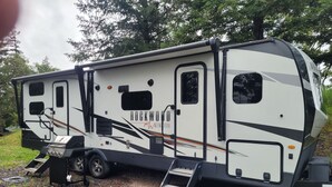 A recreational vehicle with a ramp, storage compartments, and a logo. - Cozy RV with terrific views, and peaceful surroundings. (Ukiah)