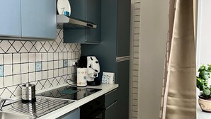 Una cucina compatta con mobili blu, un forno a microonde, una macchina da caffè e uno schienale piastrellato.