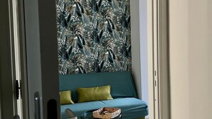 Una stanza con un divano color petrolio, una parete decorata con motivi, un lampadario e un tappeto a righe.