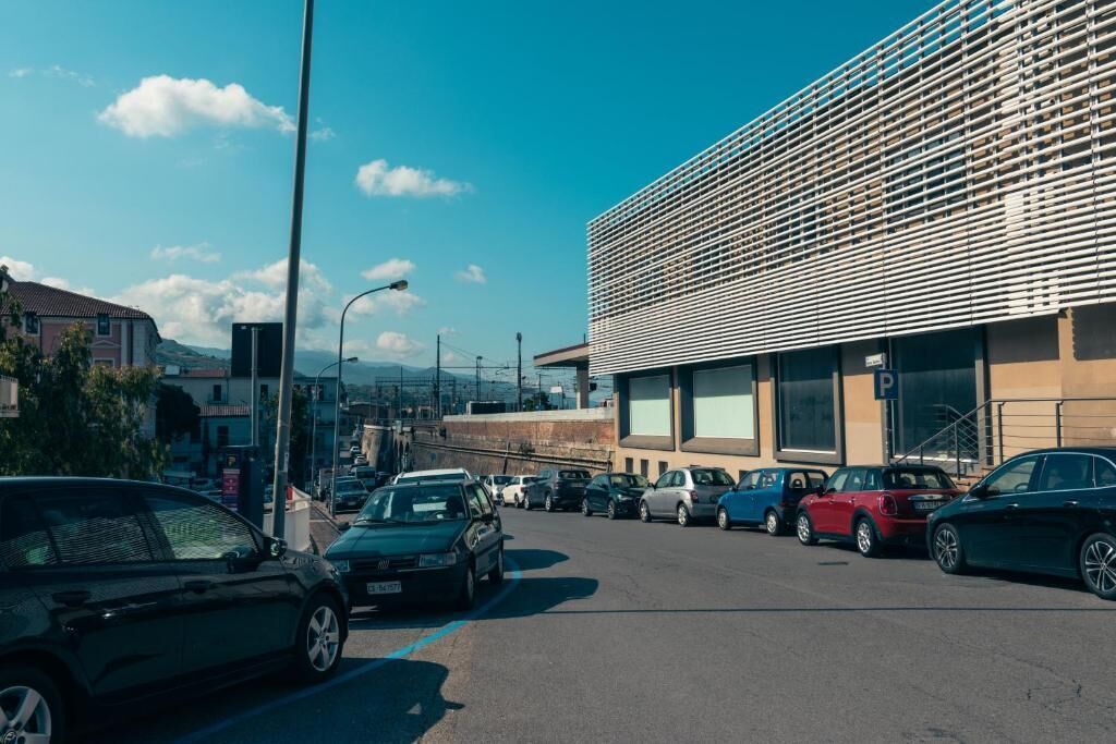 A parking lot with several cars, a modern building with a slatted facade, and a clear blue sky.