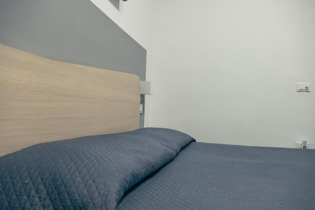 Une chambre avec une tête de lit en bois, un lit recouvert d’une courtepointe, une table de chevet et une lampe fixée au mur.