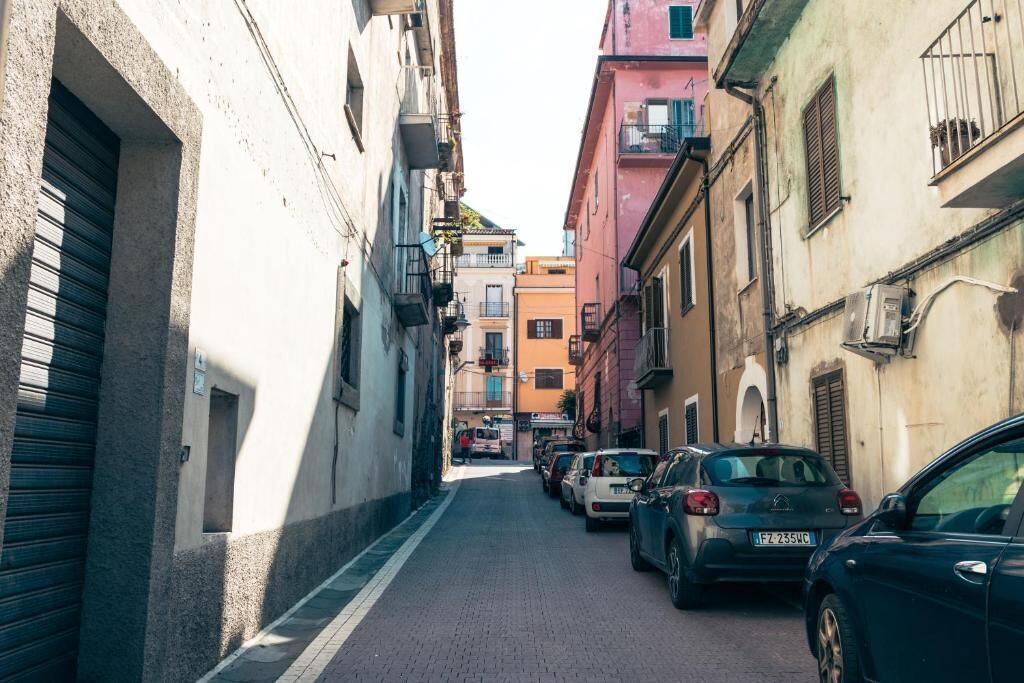 Une rue étroite bordée de voitures garées et d’immeubles aux couleurs vives.