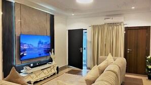 A living room with a large flat-screen TV, a beige sofa, and a decorative console table. - Eco- Eden Restination Apartment  (Lagos)
