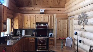 A wooden cabin interior with a kitchen featuring wooden cabinets, a stove, and a dining table with a vase. - Incredible Views - Orr Springs Rendezvous! (Ukiah)