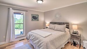 A bedroom with a large bed, a nightstand with a lamp, a window with curtains, a wall map, and a compass.