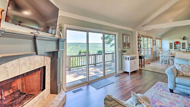 A spacious living room with a fireplace, a television, and a large sliding glass door leading to a deck with a scenic view.