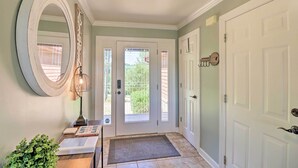 A hallway with a white door, a round mirror, a small table with a lamp, and a green plant.