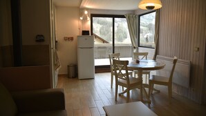 Eine kleine Küche mit einem Kühlschrank, einem Esstisch mit Stühlen und einem Fenster mit Vorhängen.